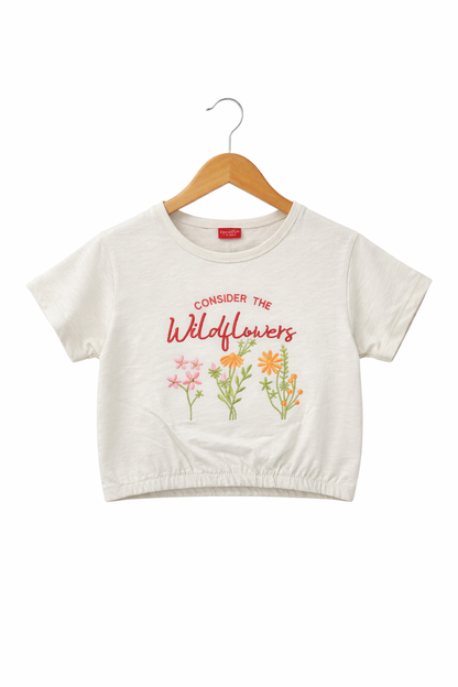 Off white girls crop t-shirt with “Consider The Wildflowers” text, floral print, elastic hem and soft cotton fabric in Pakistan.
